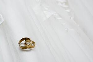 Two wedding rings laying on wedding dress photo