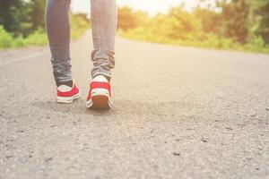 Woman feet with red sneaker shoes walking on the roadside. photo