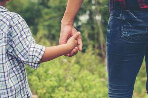 Mother holding hand of her son outdoors in summer walking on the roadside. photo