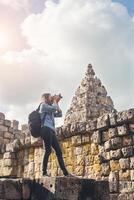 Young attractive woman photographer tourist with backpack coming to shoot photo at ancient phanom rung temple in thailand.