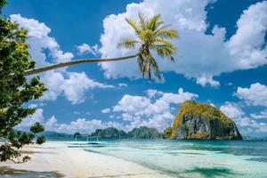 El Nido, Palawan, Philippines. Tropical scenery of exotic beach with palm tree, boat on the sandy beach and blue sky with white clouds in background