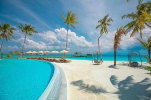 Outdoor tourism landscape. Luxurious beach resort with swimming pool and beach chairs or loungers under umbrellas with palm trees and blue sky. Summer travel and vacation background concept