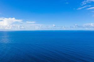 amplio panorama aéreo del océano azul profundo. relajante paisaje marino minimalista con pequeñas nubes esponjosas. vista escénica de drones de naturaleza idílica. horizonte marino sin fin, vista tranquila foto