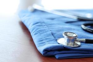 Stethoscope with blue doctor coat on wooden table with shallow DOF evenly matched and background photo