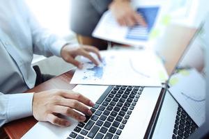 business documents on office table with smart phone and digital tablet and stylus and two colleagues discussing data in the background photo