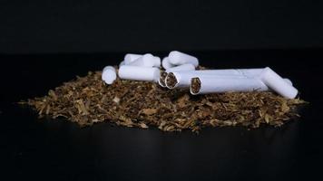 filtro de esponja de algodón para cigarrillos, montón de tabaco y algunos cigarrillos en un fondo negro foto