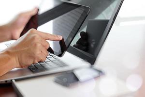 mano de hombre de negocios trabajando con tableta digital y computadora portátil en un escritorio de madera en la oficina foto