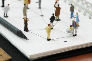 close up of miniature people with social network diagram on open notebook on wooden desk as social media concept photo