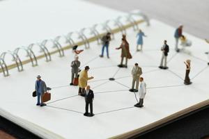 close up of miniature people with social network diagram on open notebook on wooden desk as social media concept photo