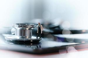 Modern medical concept-studio macro of miniature doctor with  a stethoscope and digital tablet  on wood table background photo