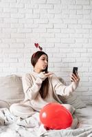 Young funny woman sitting in the bed celebrating valentine day chatting using mobile phone photo