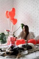 Young funny woman sitting in the bed celebrating valentine day wrapping the gifts photo