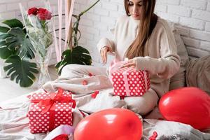 Young funny woman sitting in the bed celebrating valentine day wrapping the gifts photo