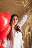 día de san valentín, día de la mujer. joven morena caucásica sentada en la cama celebrando el día de san valentín trabajando en una laptop en línea foto