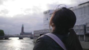 Back view of Asian woman standing and seeing beautiful view of river in Sweden, taking a deep breath and getting some fresh air, traveling abroad on holiday video