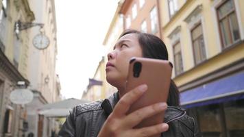 donna asiatica in piedi e utilizzando lo smartphone per vedere la mappa in città, perdersi in una piccola città, uscire per una passeggiata per strada in svezia. viaggiare all'estero in vacanza lunga video