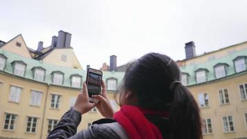 mujer asiática de pie y tomando una foto de un gran edificio amarillo en suecia en invierno, viajando al extranjero de vacaciones. usando un teléfono inteligente para tomar una foto. hermoso edificio en suecia
