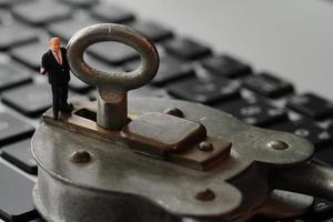 Concepto de seguridad en Internet: empresario en miniatura se para en una llave antigua y candado en el teclado de la computadora portátil foto