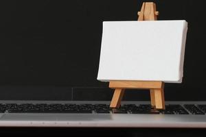 blank canvas and wooden easel on laptop computer as concept photo