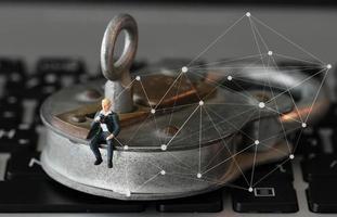 Internet security concept-miniature businessman stand on old key and padlock on laptop computer keyboard photo