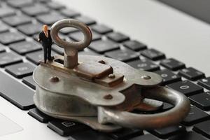 Internet security concept-miniature businessman stand on old key and padlock on laptop computer keyboard photo