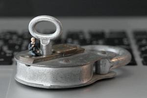 concepto de seguridad en Internet: un hombre de negocios en miniatura se sienta en una llave vieja y un candado en el teclado de una computadora portátil foto