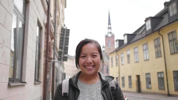 Front view of happy Asian woman standing and smiling on the street in town, going out for a walk on the street in Sweden. Traveling abroad on long holiday. Looking at camera concept