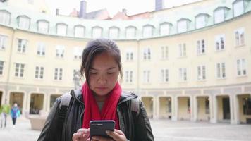 mulher asiática vestindo roupas de inverno em pé e usando smartphone na frente do prédio amarelo, digitando no smartphone. sair para passear para visitar a cidade no inverno. viajar para o exterior em férias prolongadas