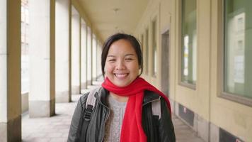 vista frontal de una mujer asiática de pie y sonriendo en el edificio, saliendo con ropa de invierno en suecia. viajar al extranjero en vacaciones largas. mirando el concepto de cámara video