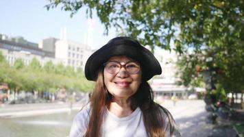 Vorderansicht einer asiatischen Frau, die in einer grünen Stadt in Schweden steht und lächelt und spazieren geht, um die Stadt in Schweden mit Bäumen und Gebäudehintergrund zu besuchen. Betrachten des Kamerakonzepts