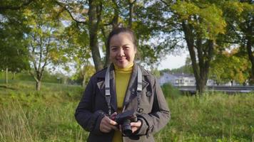 vista frontale della donna asiatica felice in piedi e sorridente nella foresta. un sacco di alberi sullo sfondo, indossando abiti invernali guardando la fotocamera in una bella giornata in vacanza, in Svezia video