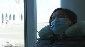 mujer asiática con mascarilla sentada y durmiendo en el aeropuerto. esperando el vuelo en el aeropuerto. sentado junto a la ventana. ir a la ciudad natal de vacaciones en avión video