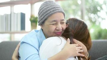 mulher paciente com câncer usando lenço na cabeça abraçando sua filha de apoio dentro de casa, conceito de saúde e seguro. video