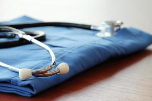 Stethoscope with blue doctor coat on wooden table with shallow DOF evenly matched and background photo