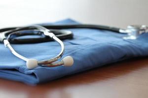 Stethoscope with blue doctor coat on wooden table with shallow DOF evenly matched and background photo