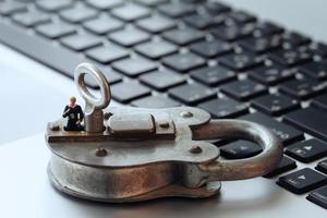 Internet security concept-miniature businessman stand on old key and padlock on laptop computer keyboard photo