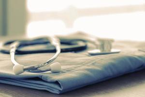 Stethoscope with blue doctor coat on wooden table with shallow DOF evenly matched and background photo