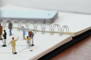 close up of miniature people with social network diagram on open notebook on wooden desk as social media concept photo