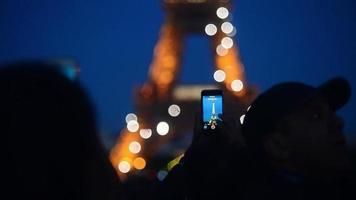 il tour eiffel illumina la folla di persone che fanno foto con il telefono cellulare - Parigi notturna video