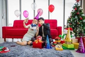 Asian couple lover are giving a gift box and taking a selfie by mobile smartphone with Christmas gift in Christmas holiday and happy new year patty