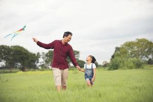 Asian child girl and father with a kite running and happy on meadow in summer in nature photo