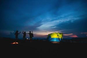 grupo de siluetas de amigos asiáticos turistas bebiendo y tocando guitarra juntos con felicidad en verano mientras acampan cerca del lago foto