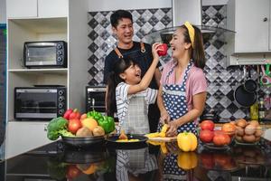 familia feliz tiene a papá, mamá y su pequeña hija cocinando juntos en la cocina foto