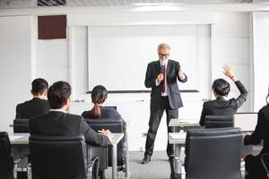 Business Audience raising hand up while businessman is speaking in training for Opinion with Meeting Leader in Conference Room