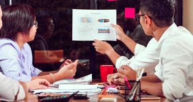 Asian businessmen and businesswomen analysis documents on office table with laptop computer and graph financial diagram working in the background photo