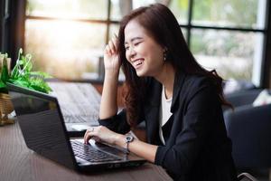 mujeres de negocios asiáticas sonriendo y usando un cuaderno para trabajar en una cafetería foto