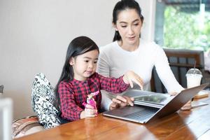 Mom is teaching her daughter to read a book and playing notebook. photo