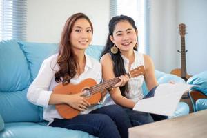 Two women are having fun playing ukulele and smiling at home for relax time photo