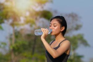 mujer deportiva agua potable asiática al aire libre en un día soleado foto