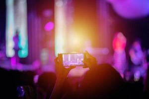 siluetas de la multitud de conciertos en la vista trasera de la multitud del festival levantando la mano y usando un teléfono inteligente para tomar fotos y videos en luces brillantes del escenario